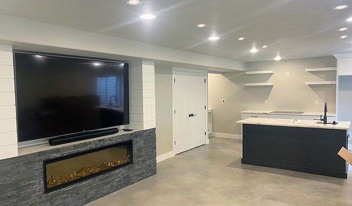 A renovated basement with a large television in the middle of the room. Perfect for basement renovations or a basement remodel.