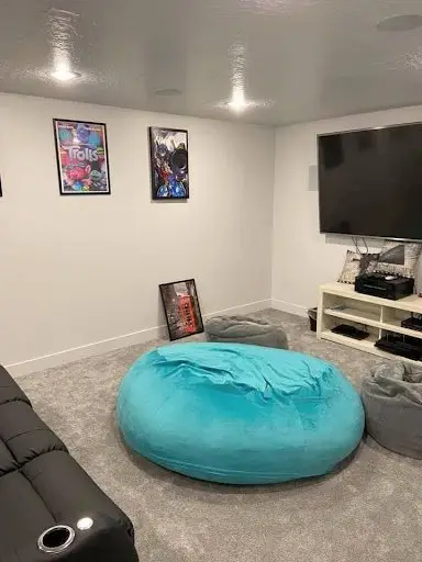 Cozy man cave in a finished basement with modern decor, featuring a large bean bag, framed wall art, and a home entertainment setup—transformed from an unfinished basement.
