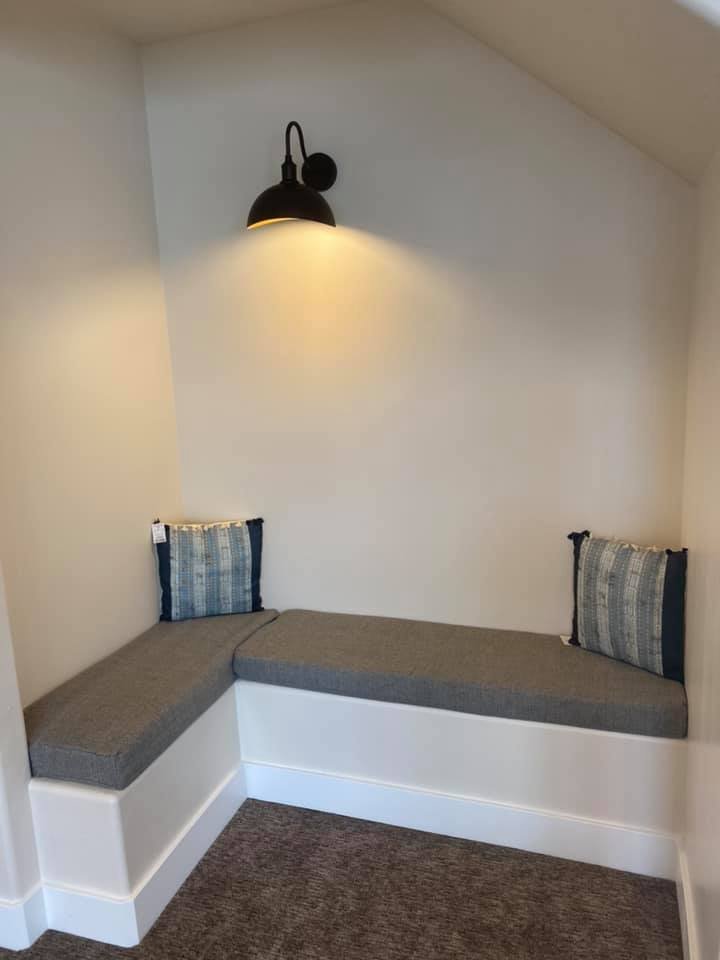 Corner of a room with a built-in gray cushioned bench, two striped pillows, and a black wall sconce.