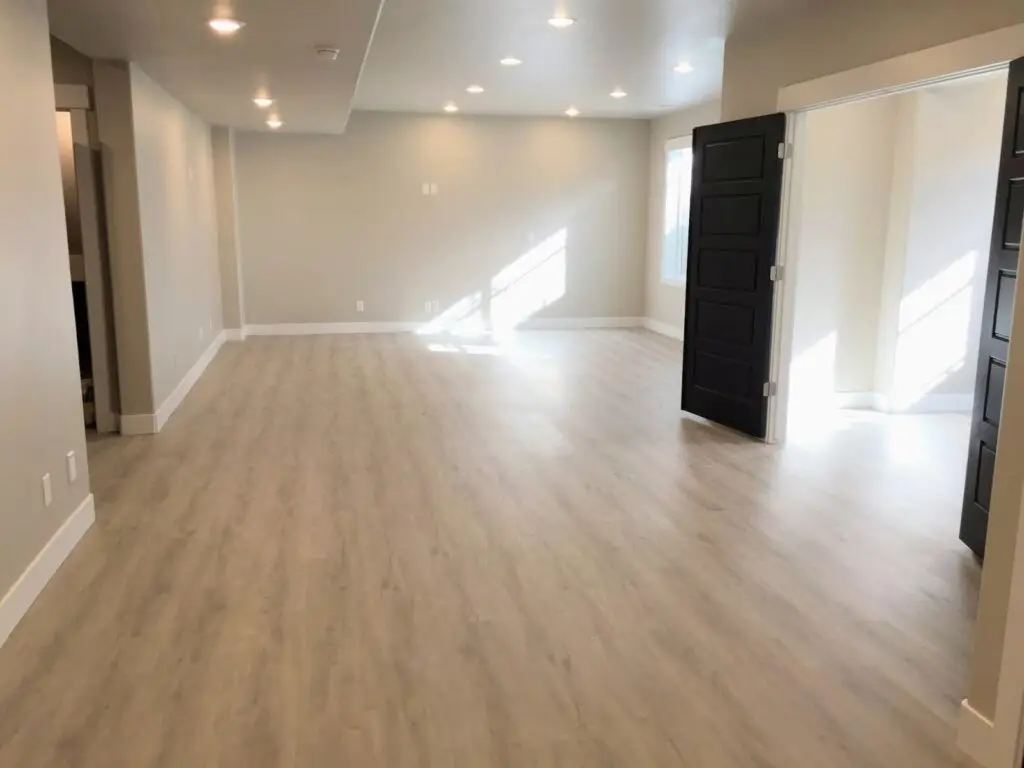 Empty room with light wood flooring, beige walls, recessed lighting, and black double doors. - Creative Construction Solutions Empty room with light wood flooring, beige walls, recessed lighting, and black double doors.