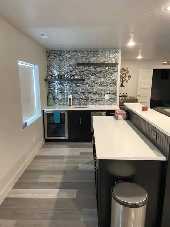 A modern kitchen with mosaic backsplash, white counter, and gray flooring. - Creative Construction Solutions A modern kitchen with mosaic backsplash, white counter, and gray flooring.